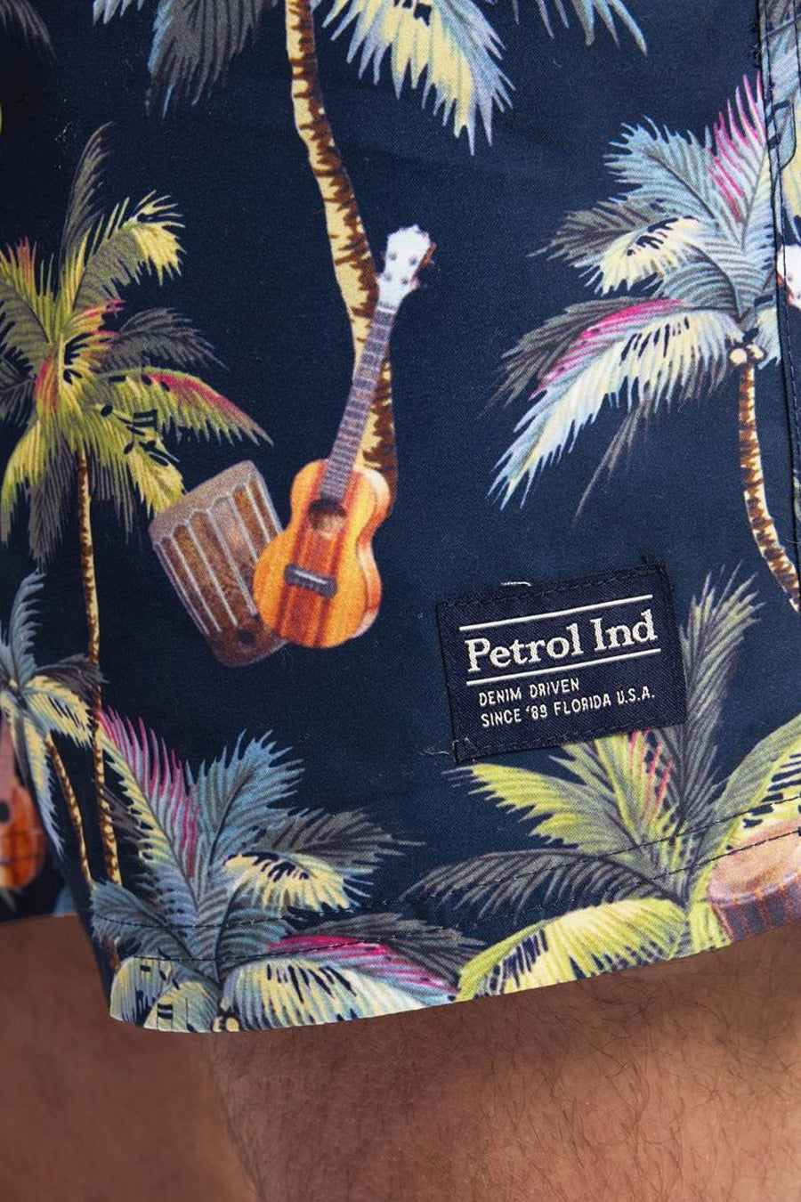 Blauwe zwembroek van Petrol Industries met kleurrijk tropisch patroon van palmbomen, ukelele en drums.