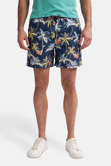 Marineblauwe zwembroek van Petrol Industries® met palmboom- en gitaarmotief, gedragen met een groen T-shirt en witte schoenen.