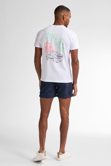T-shirt à manches courtes blanc par Petrol Industries® avec un motif imprimé au dos, porté avec un short bleu marine et des baskets blanches.