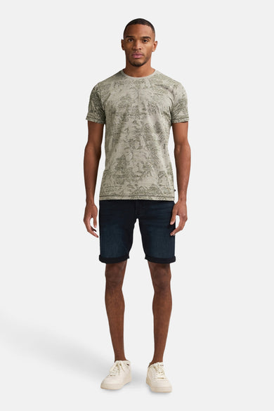 Groen T-shirt met korte mouwen van Petrol Industries® met textuurprint, gedragen met een donkerblauwe spijkerbroek en crèmekleurige sneakers.