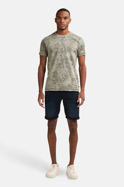 Groen T-shirt met korte mouwen van Petrol Industries® met textuurprint, gedragen met een donkerblauwe spijkerbroek en crèmekleurige sneakers.