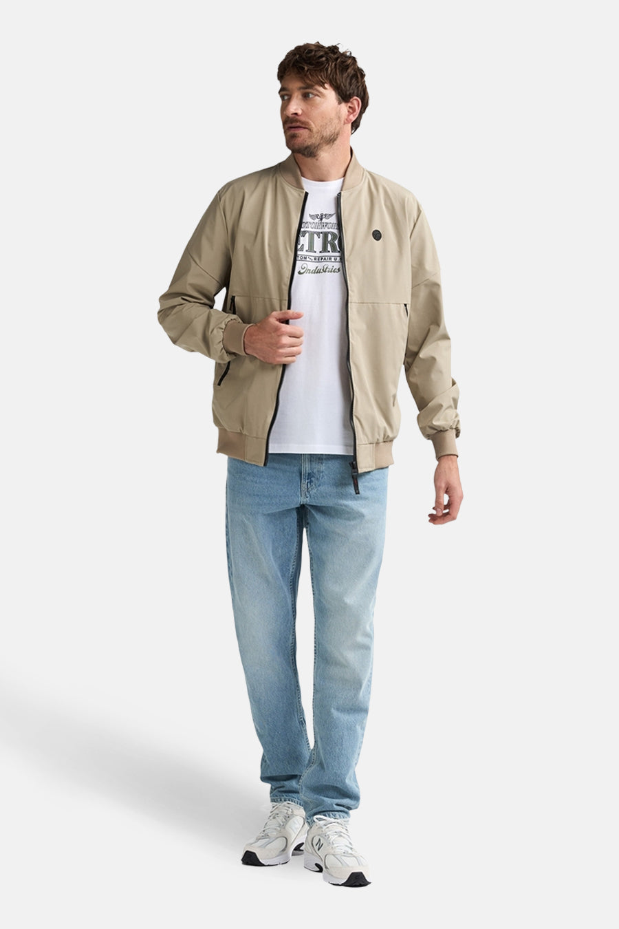 Korte beige jas van Petrol Industries, met ritssluiting over een wit T-shirt en een blauwe jeans.
