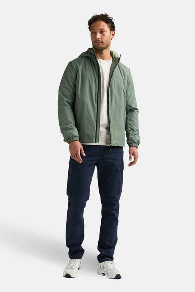 Lange kaki jas van Petrol Industries®, gedragen met een marineblauwe cargobroek en witte sneakers.