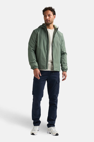 Lange kaki jas van Petrol Industries®, gedragen met een marineblauwe cargobroek en witte sneakers.