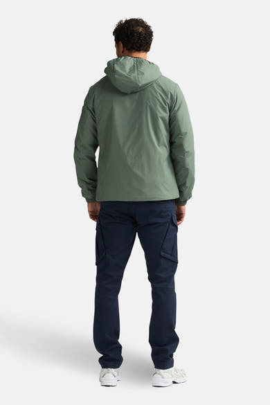 Veste longue kaki de Petrol Industries®, avec capuche et poches cargo, portée avec un pantalon bleu marine et des baskets blanches, vue de dos.
