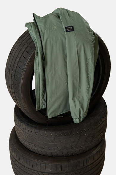 Lange kaki jas van Petrol Industries, liggend op een stapel zwarte banden.