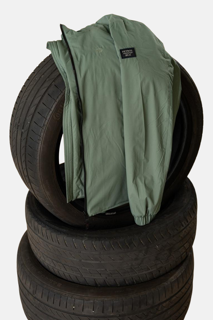 Lange kaki jas van Petrol Industries, liggend op een stapel zwarte banden.
