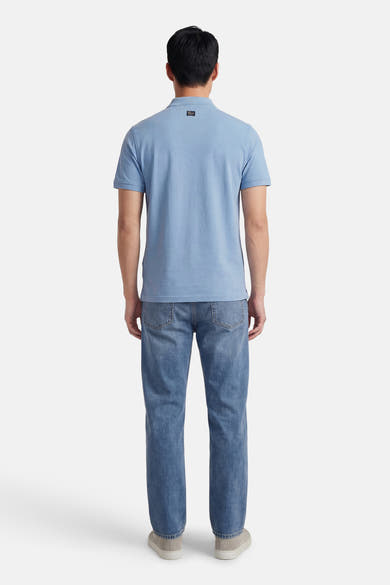 Polo bleu à manches courtes de Petrol Industries, avec un écusson sur le col et porté avec un jean décontracté.