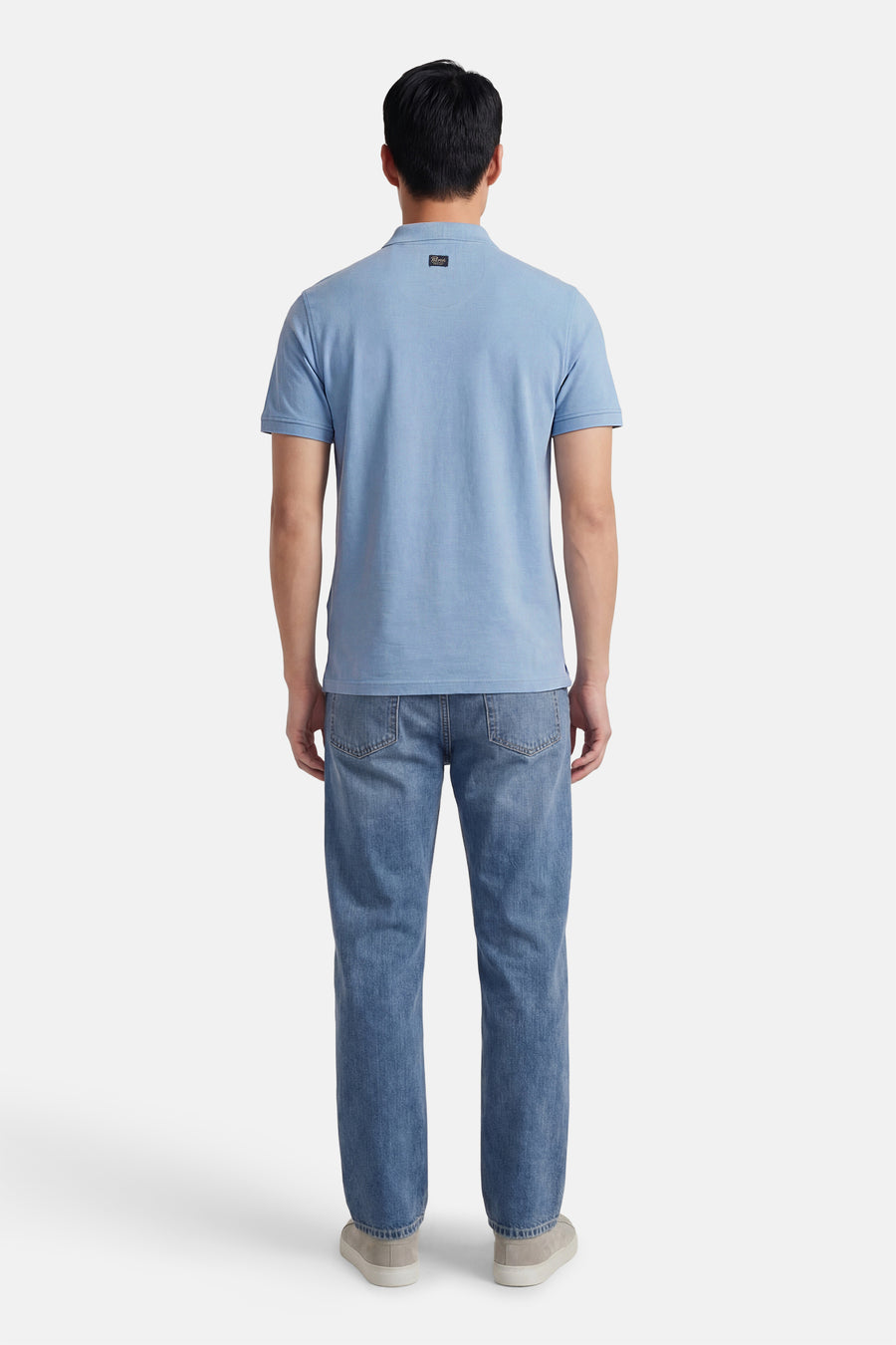 Polo bleu à manches courtes de Petrol Industries, avec un écusson sur le col et porté avec un jean décontracté.