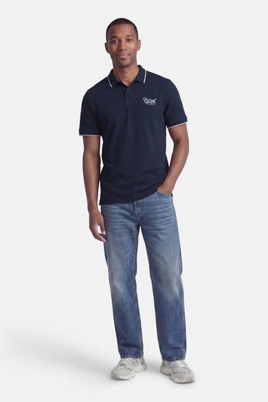 Polo à manches courtes bleu de Petrol Industries, avec col et manches à bordure blanche, porté avec un jean et des baskets.