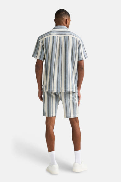 Short bleu rayé de Petrol Industries, porté avec une chemise assortie, et des baskets blanches.