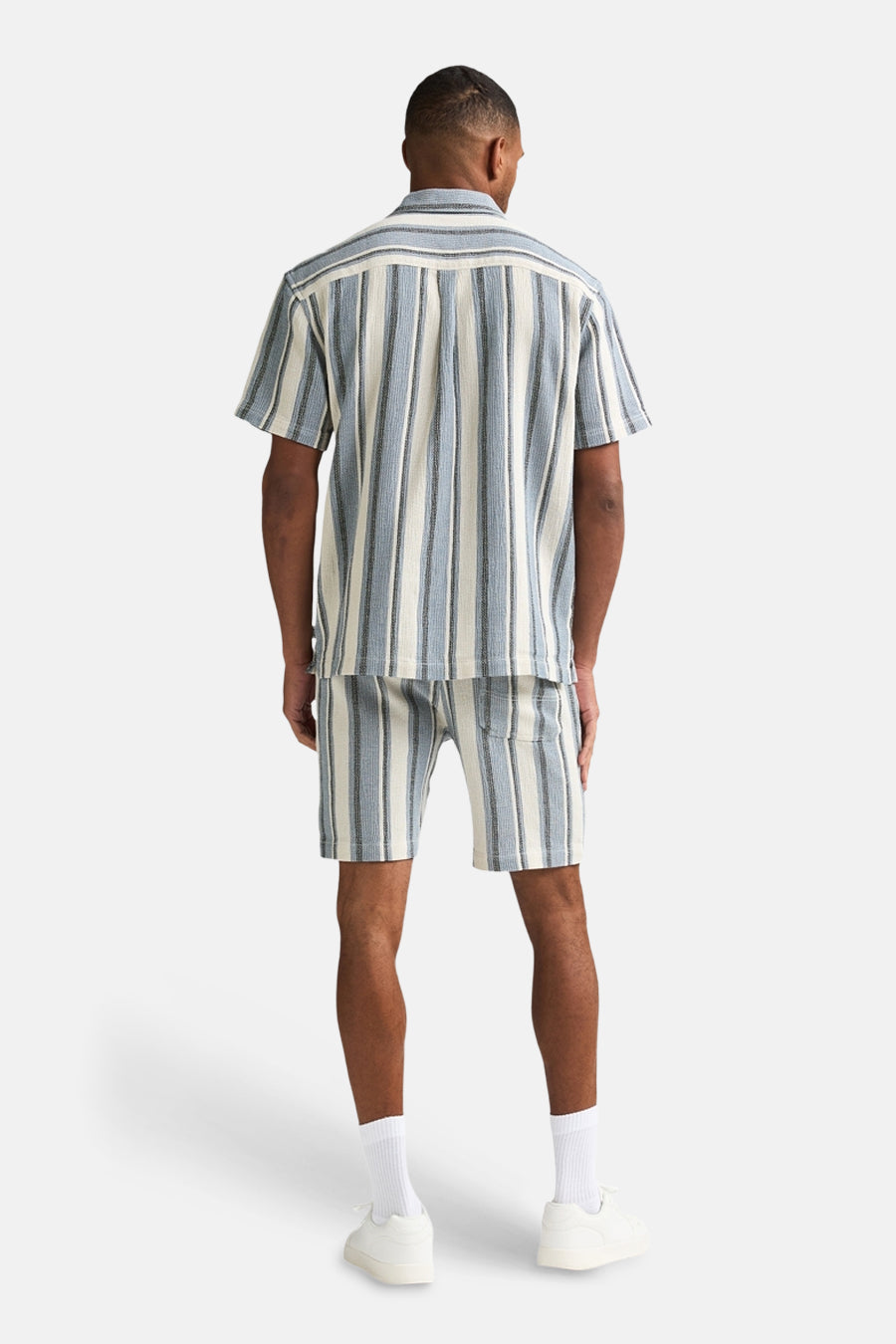 Short bleu rayé de Petrol Industries, porté avec une chemise assortie, et des baskets blanches.