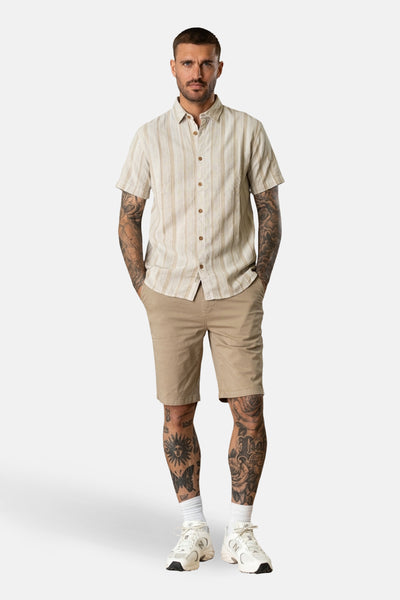Chemise beige à manches courtes de Petrol Industries®, à rayures verticales, portée avec un short kaki et des baskets blanches.