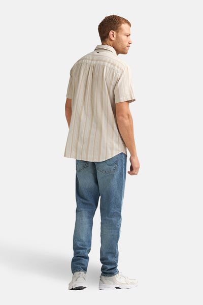 Chemise beige rayée de Petrol Industries, vue de dos, portée avec un jean bleu et des chaussures de sport blanches.