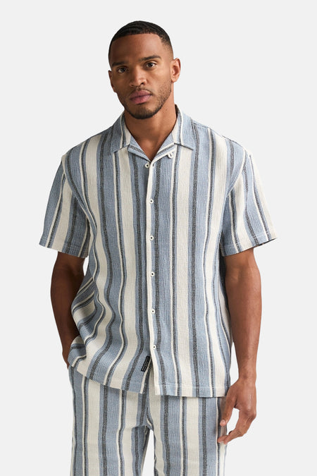 Chemise à manches courtes bleue à rayures verticales de Petrol Industries, portée par un homme, faisant partie d'un ensemble assorti.