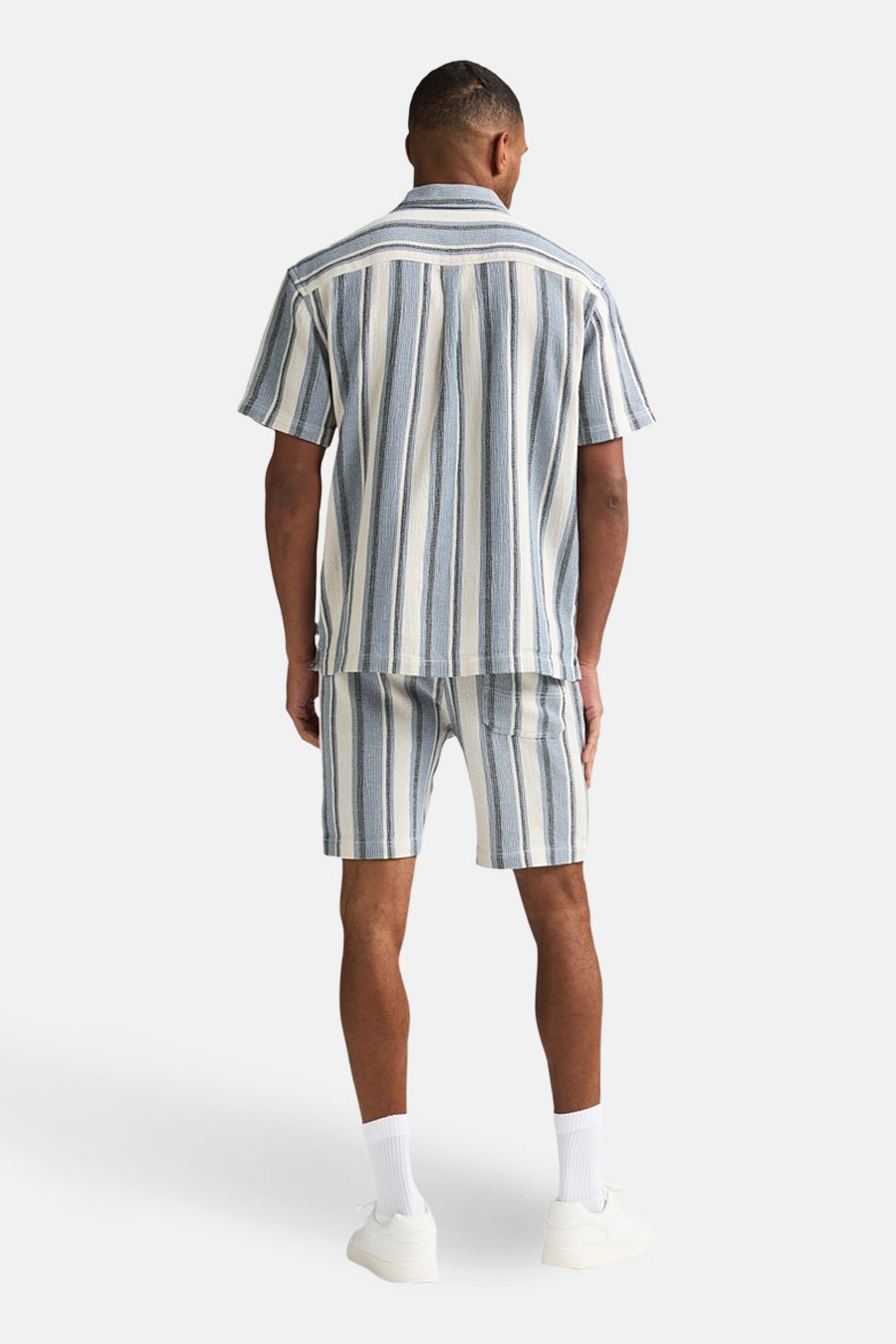 Chemise à manches courtes bleue à rayures par Petrol Industries, vue de dos avec des chaussettes et des chaussures blanches.