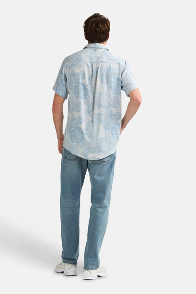 Chemise à manches courtes bleue de Petrol Industries avec motif floral, portée de dos avec un jean et des baskets.