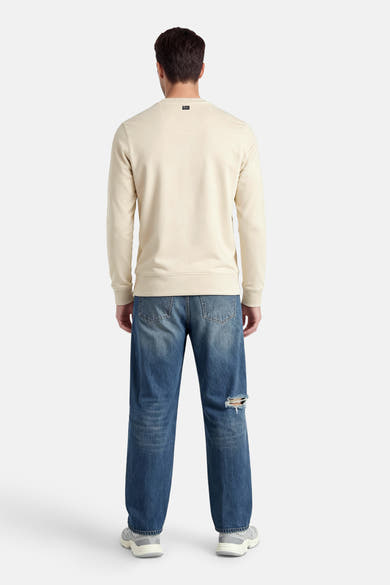 Sweat-shirt écru de Petrol Industries, avec un petit logo dans le cou, porté avec un jean délavé et des chaussures de sport.