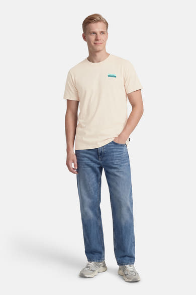 T-shirt à manches courtes écru de Petrol Industries, avec un logo imprimé discret sur la poitrine, porté avec un jean bleu.
