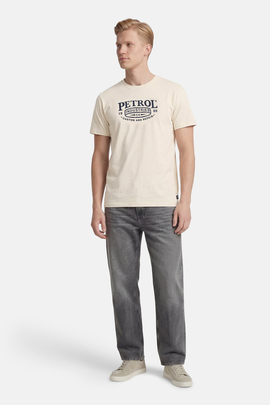 T-shirt écru à manches courtes de Petrol Industries, avec un imprimé graphique sur le devant, porté avec un jean gris et des baskets.