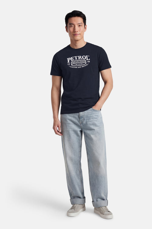 T-shirt à manches courtes bleu de Petrol Industries, porté avec un jean ample délavé et des baskets grises.
