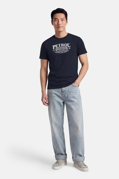 T-shirt à manches courtes bleu de Petrol Industries, porté avec un jean ample délavé et des baskets grises.