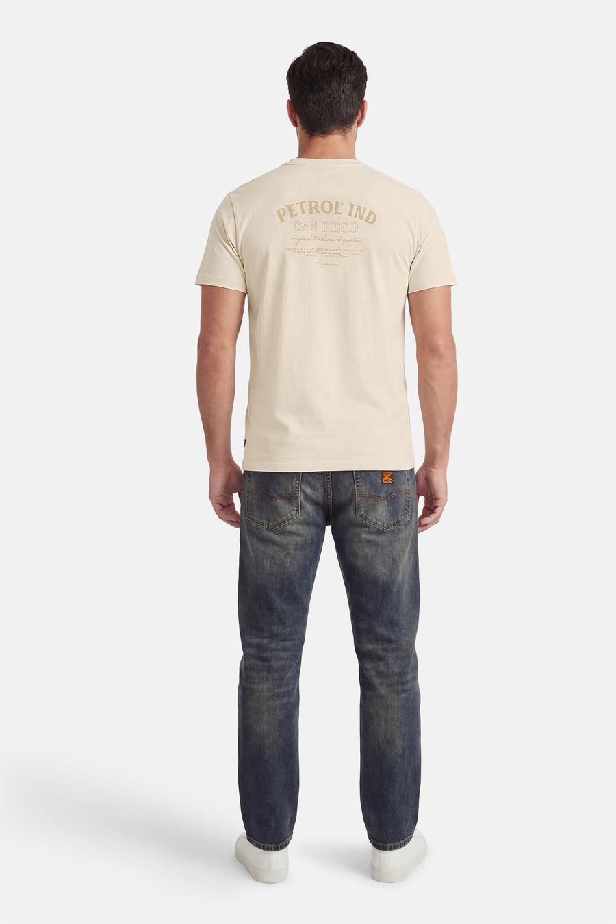 Ecru T-shirt met korte mouwen van Petrol Industries, met een decoratieve tekstprint op de rug, gedragen met een blauwe jeans en witte sneakers.