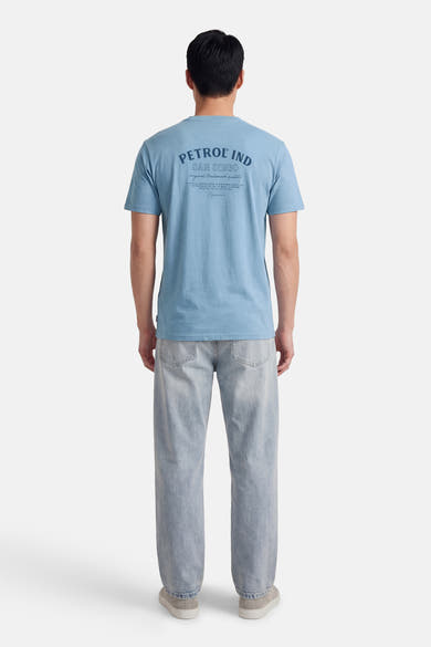 T-shirt bleu à manches courtes de Petrol Industries®, avec un imprimé sur le dos, porté avec un jean décontracté.