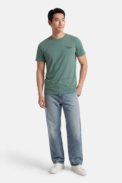 T-shirt à manches courtes vert de Petrol Industries, porté avec un jean bleu et des baskets blanches.