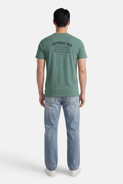 T-shirt vert à manches courtes de Petrol Industries, avec un imprimé noir dans le dos, porté avec un jean délavé.