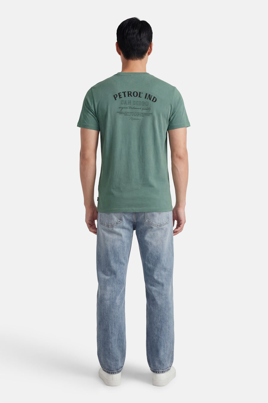 T-shirt vert à manches courtes de Petrol Industries, avec un imprimé noir dans le dos, porté avec un jean délavé.