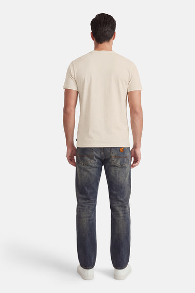 T-shirt à manches courtes écru de Petrol Industries®, porté avec un jean bleu foncé et des baskets blanches.