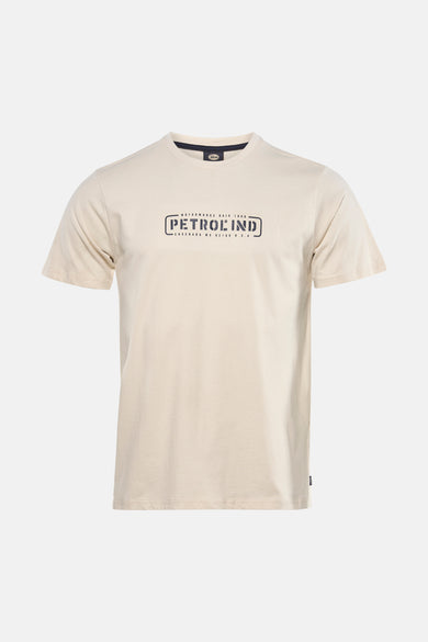 Ecru T-shirt met korte mouwen van Petrol Industries, met een grafisch logo op de voorkant, gedragen met een wijde jeans en sportschoenen.