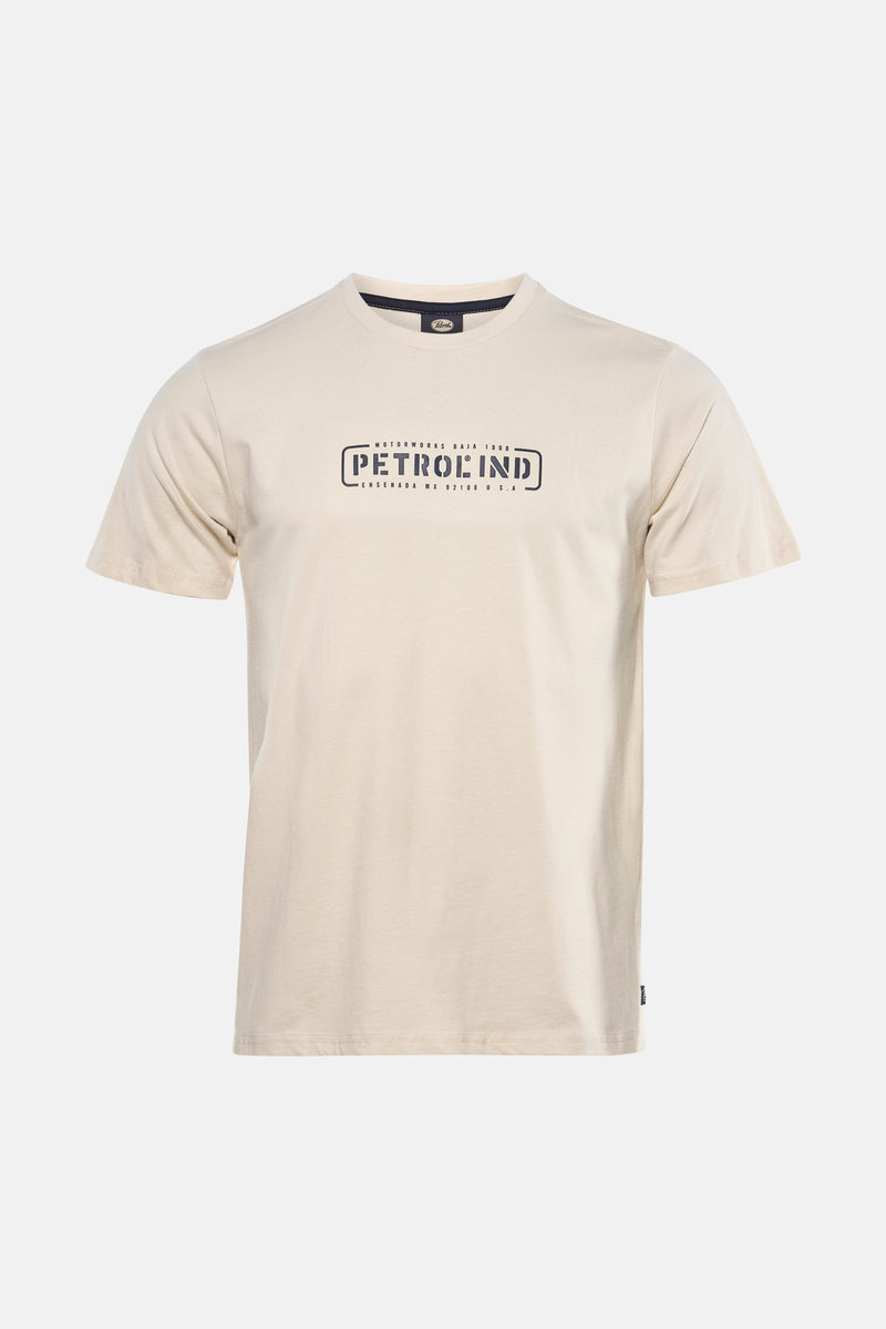 Ecru T-shirt met korte mouwen van Petrol Industries, met een grafisch logo op de voorkant, gedragen met een wijde jeans en sportschoenen.