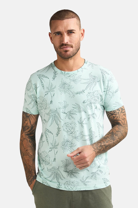 T-shirt vert à manches courtes de Petrol Industries®, avec motif fleuri intégral et homme tatoué portant un pantalon kaki.