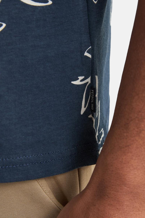 T-shirt bleu à manches courtes de Petrol Industries, avec un motif blanc et porté avec un pantalon beige.