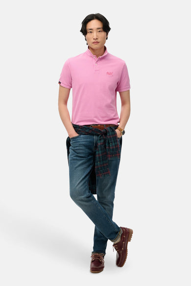 Polo roze met korte mouwen van SUPERDRY, gedragen met een jeansbroek en een geruitte shirt.