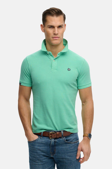 Polo vert en coton, de Superdry, porté avec un jean et une ceinture en cuir.