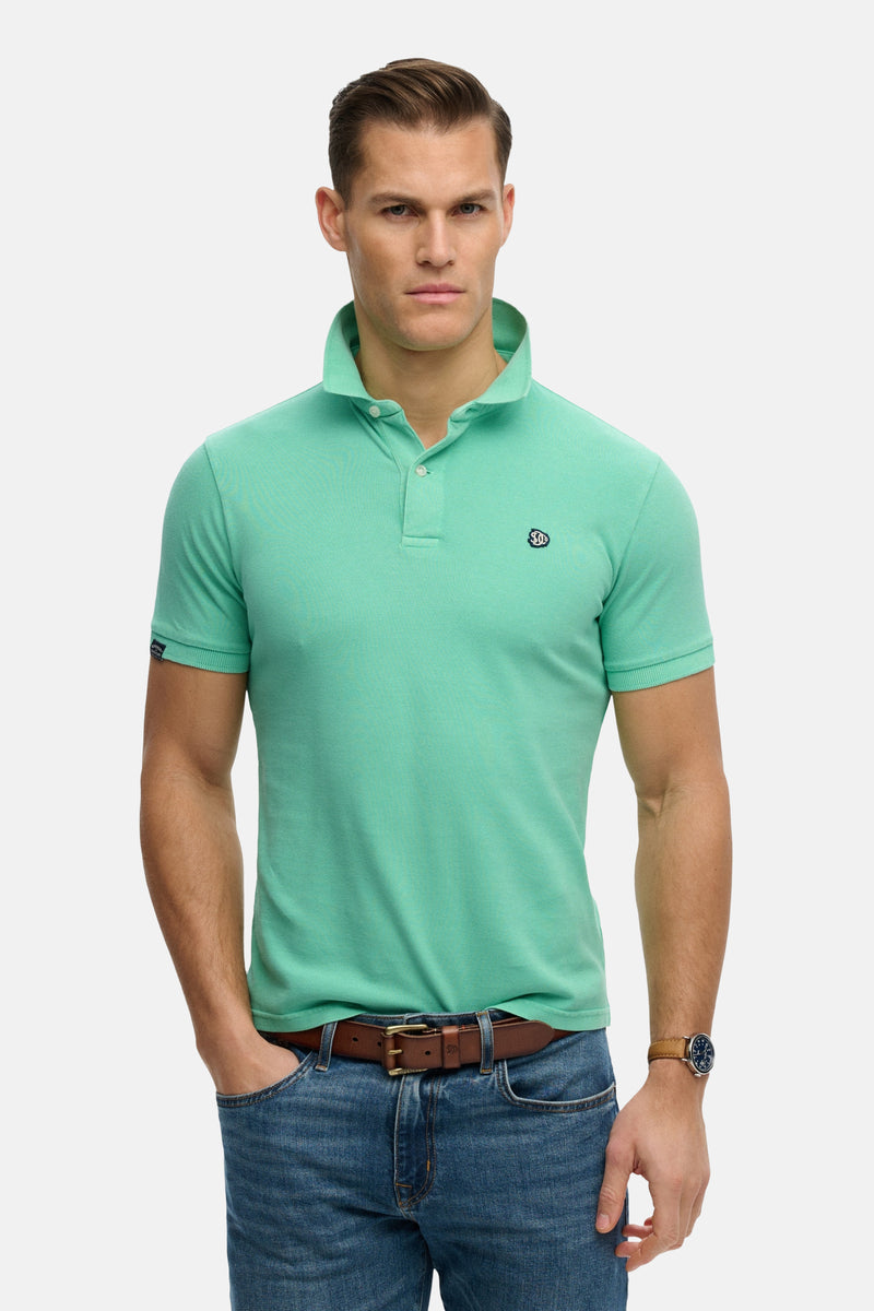 Polo vert en coton, de Superdry, porté avec un jean et une ceinture en cuir.