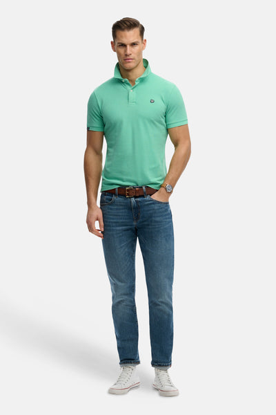 Polo vert de SUPERDRY, porté avec un jean bleu, une ceinture marron et des baskets blanches.