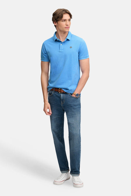 Polo bleu foncé à manches courtes par SUPERDRY, col boutonné, petit logo brodé, porté avec jeans et baskets blanches, vue de face.