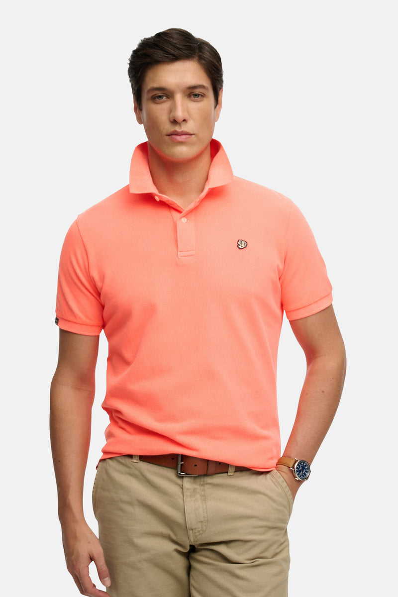 Koraalrode polo van SUPERDRY van achteren gezien, met een kraag, een vierkante pas achter op de nek, en een kaki korte broek.