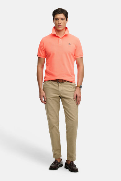 Koraalkleurig poloshirt van SUPERDRY met kraag, twee knopen en logo op de borst, gedragen met een beige chino en bruine loafers.