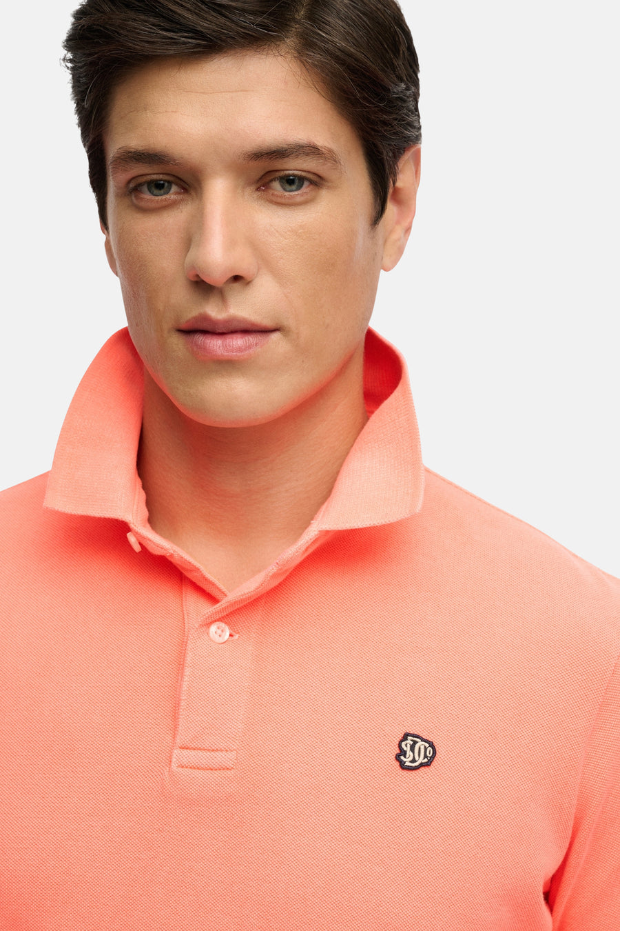 Koraalkleurig poloshirt van SUPERDRY met pique-textuur, twee knopen en geborduurd logo op de borst.