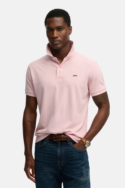 Polo rose à manches courtes de SUPERDRY, porté avec un jean et une ceinture en cuir tressé.