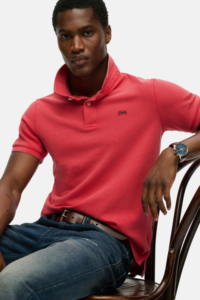 Roze poloshirt met korte mouwen van SUPERDRY, gedragen met een blauwe spijkerbroek en een bruine riem.