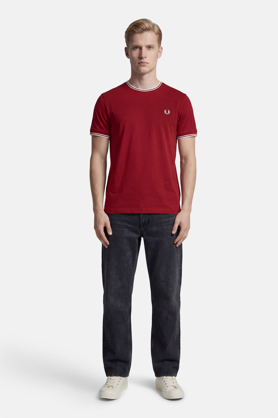 T-shirt rouge à manches courtes de Fred Perry, avec un col et des bords de manches rayés, porté avec un jean noir et des baskets blanches.