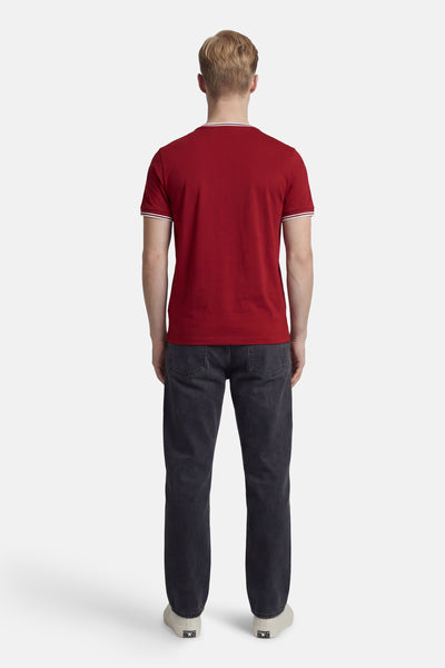 Rood T-shirt met korte mouwen van FRED PERRY, met witte strepen op de kraag en mouwen, gedragen met een grijze jeans.