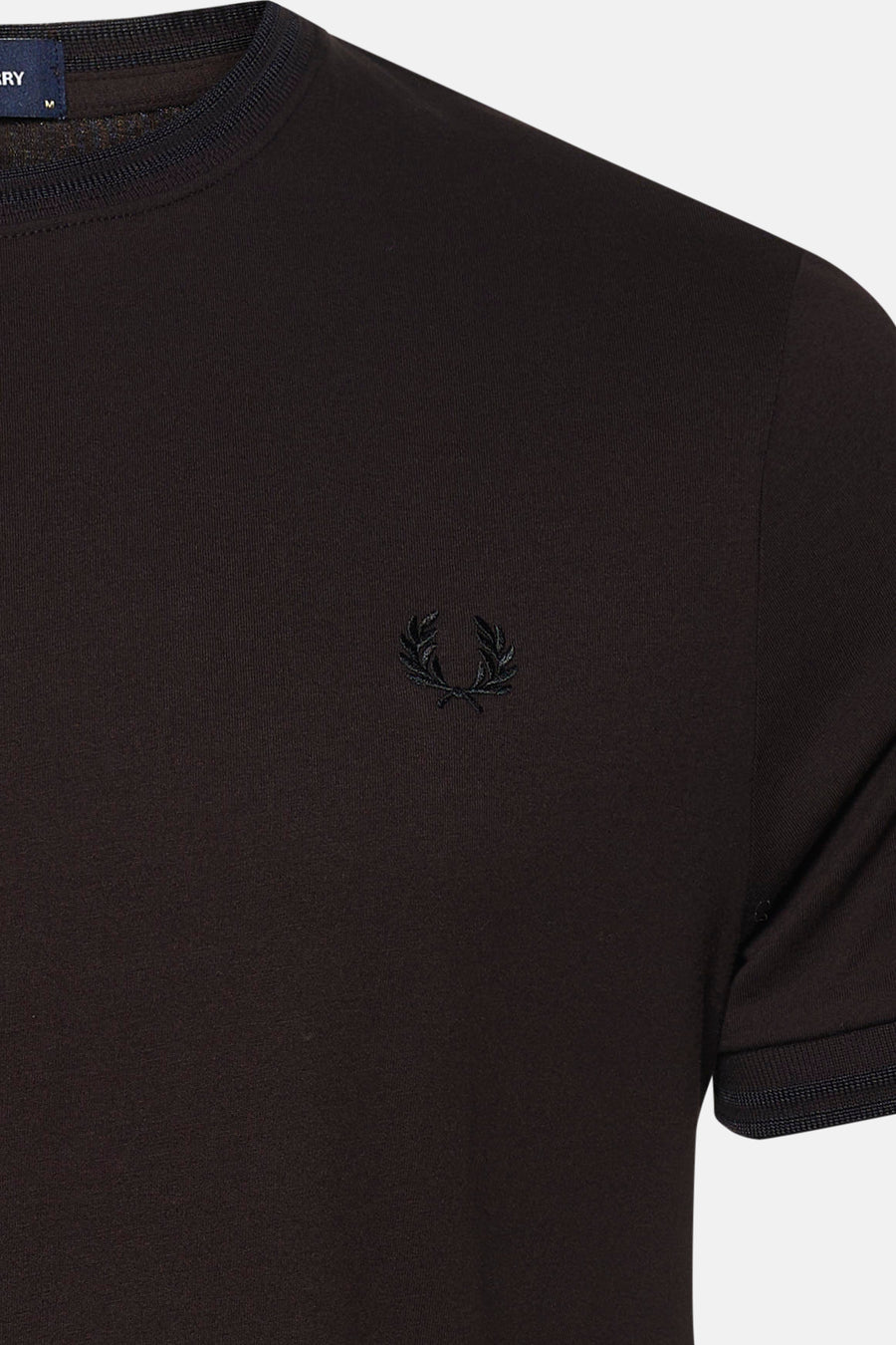 Détail d’un T-shirt à manches courtes brun FRED PERRY avec col rond, manches bordées et logo brodé.