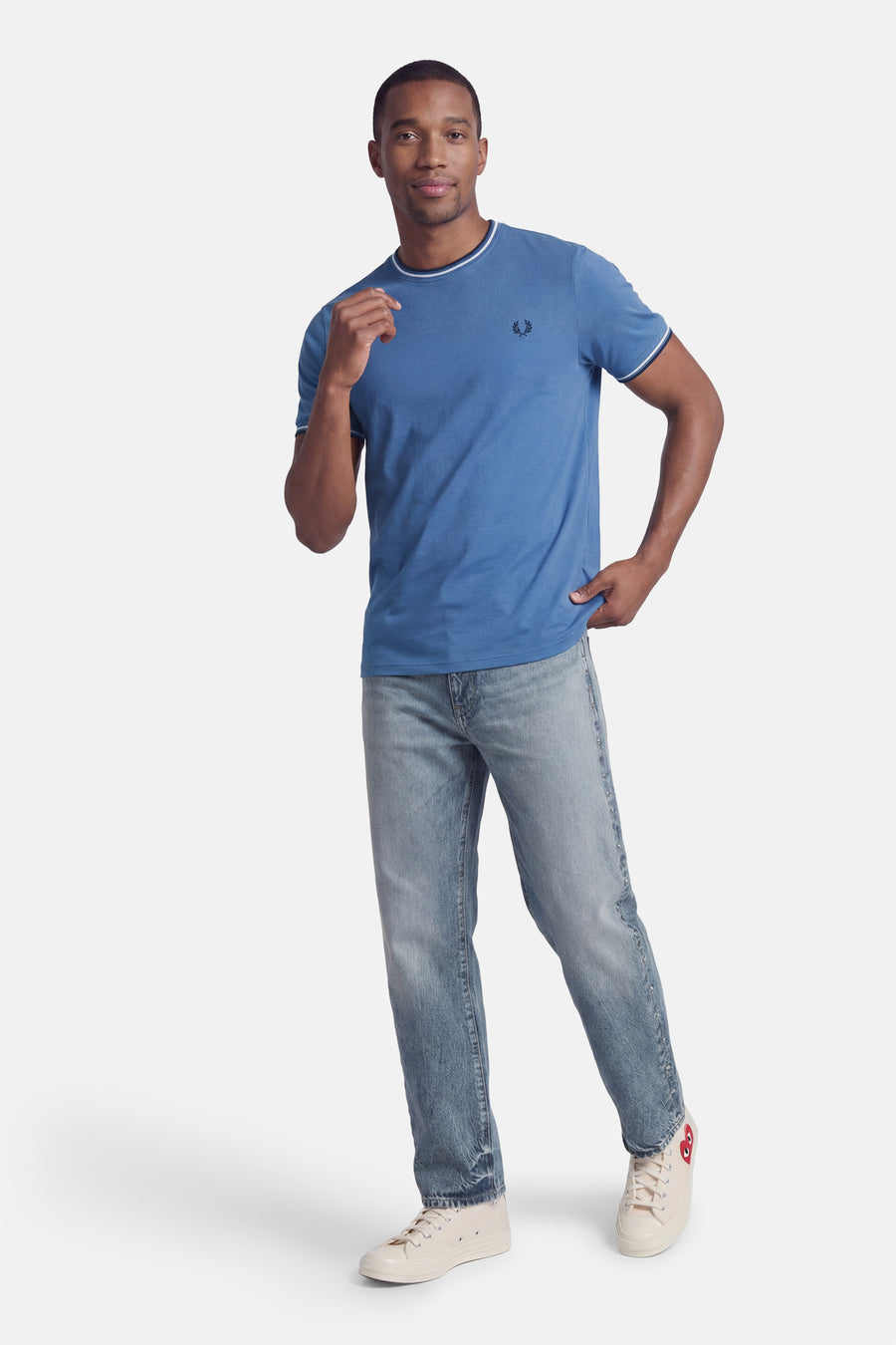 T-shirt bleu à manches courtes de FRED PERRY, porté avec un jean délavé et des baskets en toile.